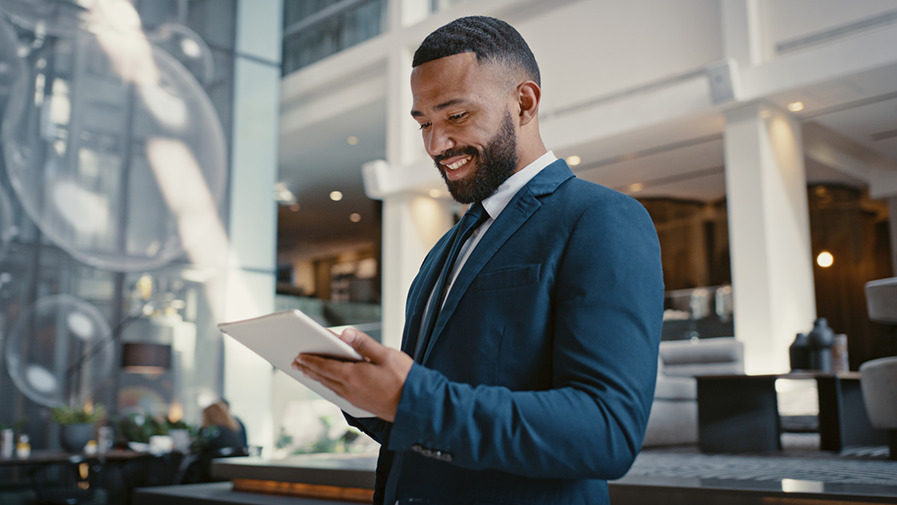 A man wearing a suit in a smart hotel lobby looks down at a tablet device