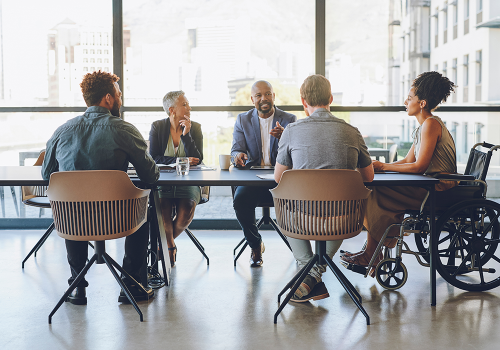 A diverse group sit a a meeting table in discussion