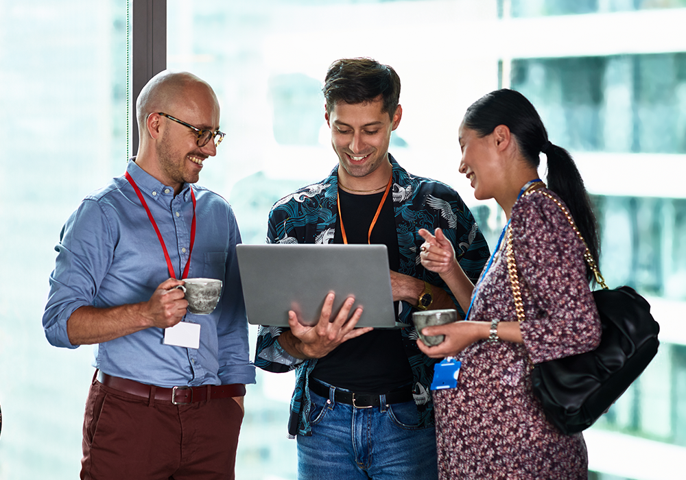 3 people smile whilst looking at a laptop