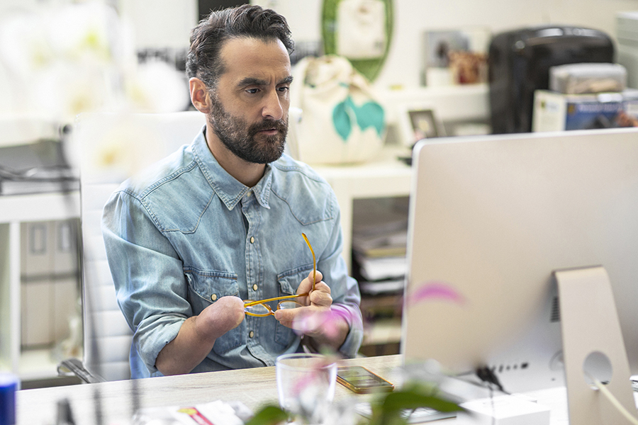 Serious mature businessman looking at computer. Disabled design professional sitting at desk. He is in creative office.