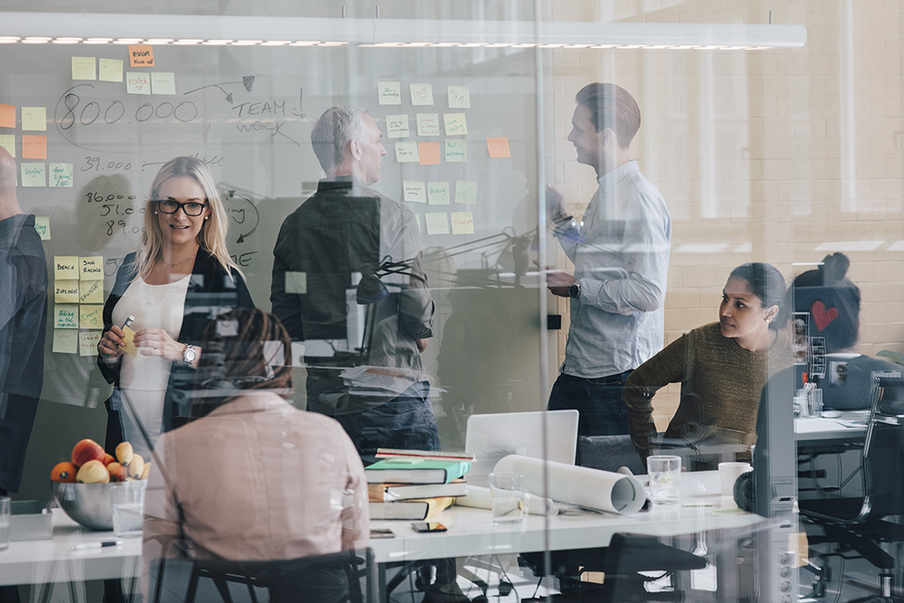 Multi-ethnic team planning during meeting in board room at office seen from glass