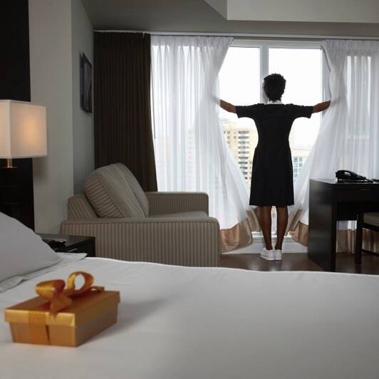 Chambermaid opening curtains, box of chocolates on guest's bed