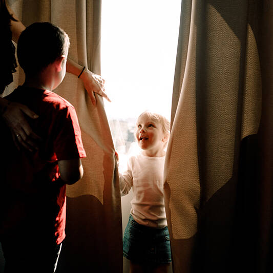 Girl standing by window looking at mother with boy in hotel room