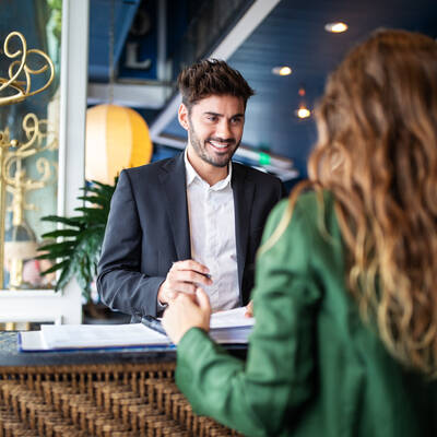 Male hotel receptionist helping a woman guest in checking in process. Woman in hotel check-in at reception talking with the concierge at front office