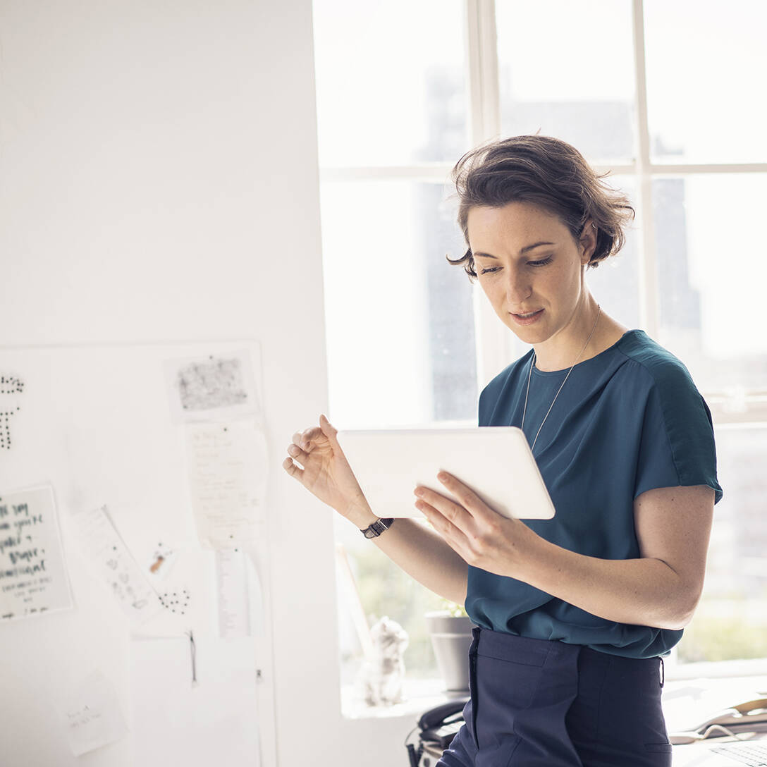 A photo of businesswoman using digital tablet in creative office. Female expert is holding technology. She is leaning on table at workplace.